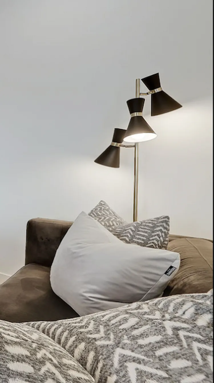 Editorial interior detail of a Renfrew multi-level home, black tri-cone floor lamp beside a brown velvet sofa with patterned cushions